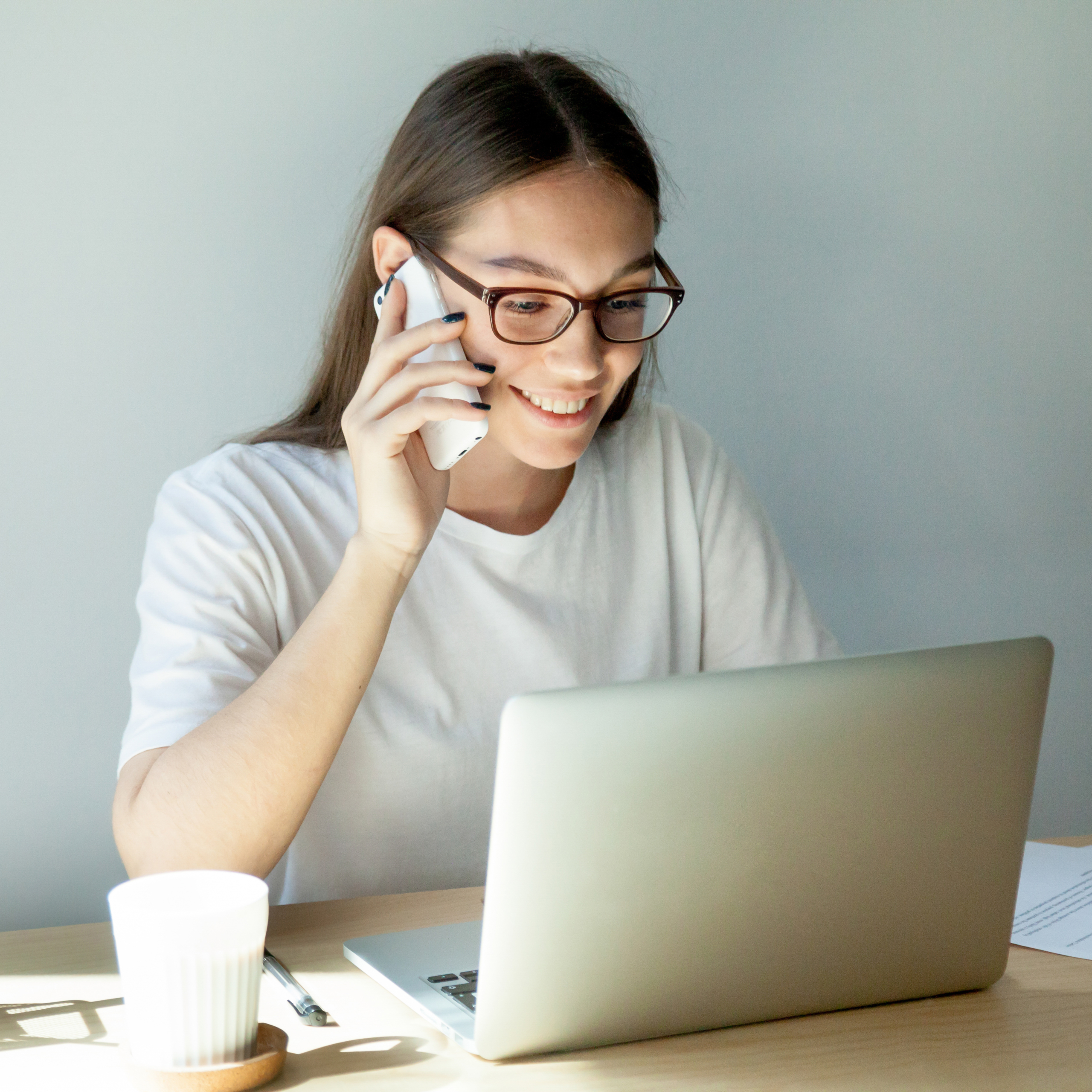 Millennial woman in glasses talking on mobile and using laptop